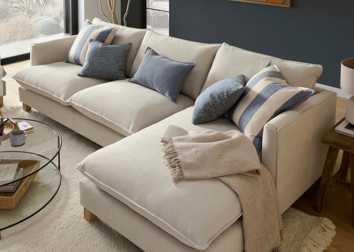 A lifestyle image of the Howth linen rhf corner chaise with blue and stripe scatters and a blanket.