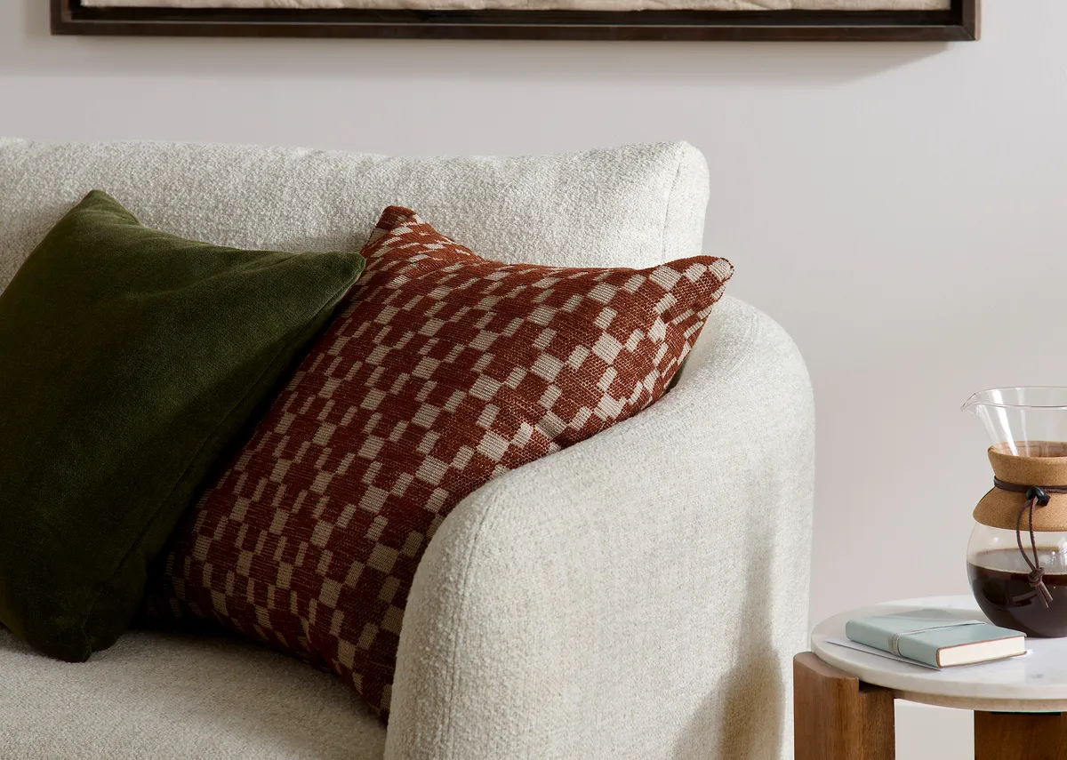 A closeup view of yje rust brown cross print cushion and plain green velvet cushion that come with the sofa.