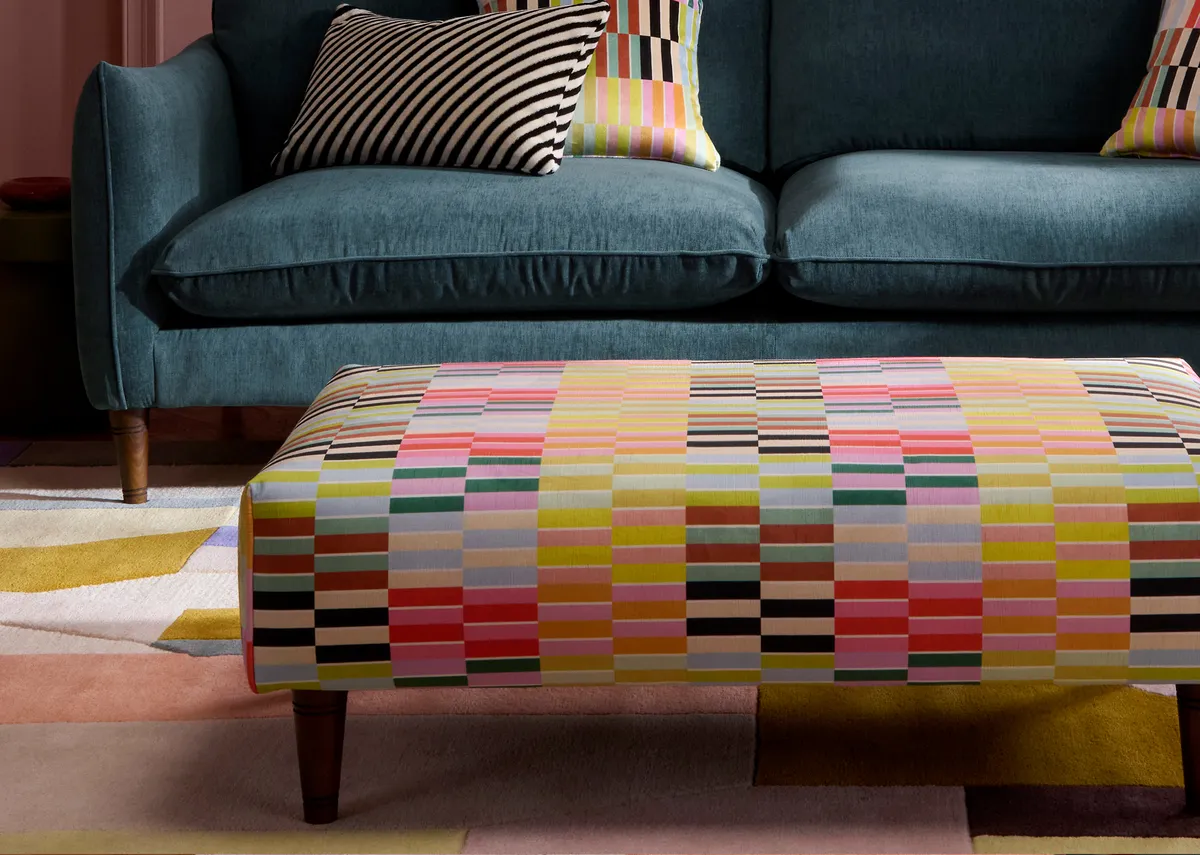 A lifestyle closeup image of the Kenmare multi stripe footstool with blue fabric sofa.