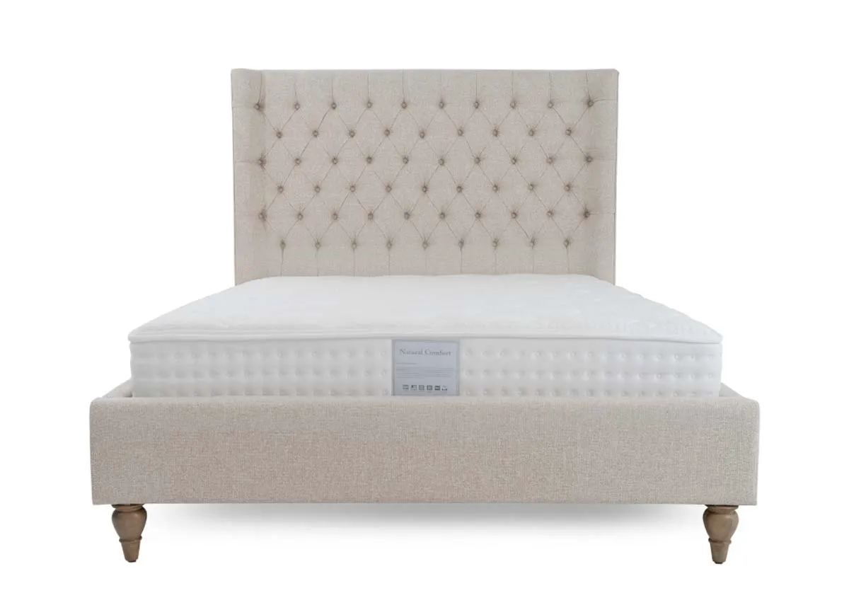 A cream fabric bed frame from EZ Livings Chelsea range. Front view of tufted button headboard with winged sides