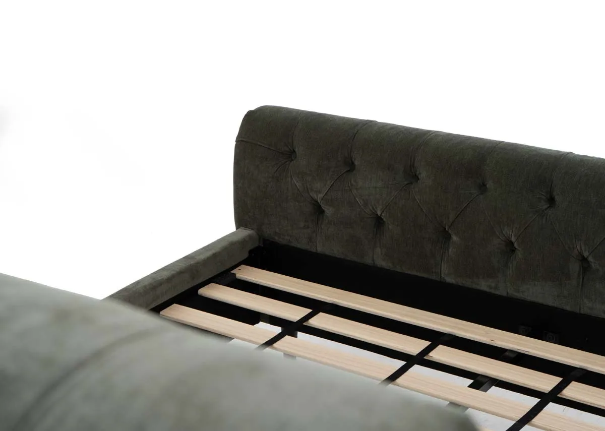 A green fabric bedframe with tufted Chesterfield detail and scrolled finish head and footboard. Closeup of the footboard and slat wood base