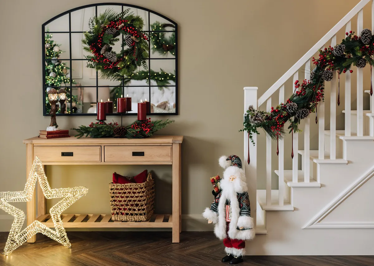 A lifestyle image of the Albany console with Meera Mirror and Berry and cone wreath with Santa at the bottom of the staircase. 