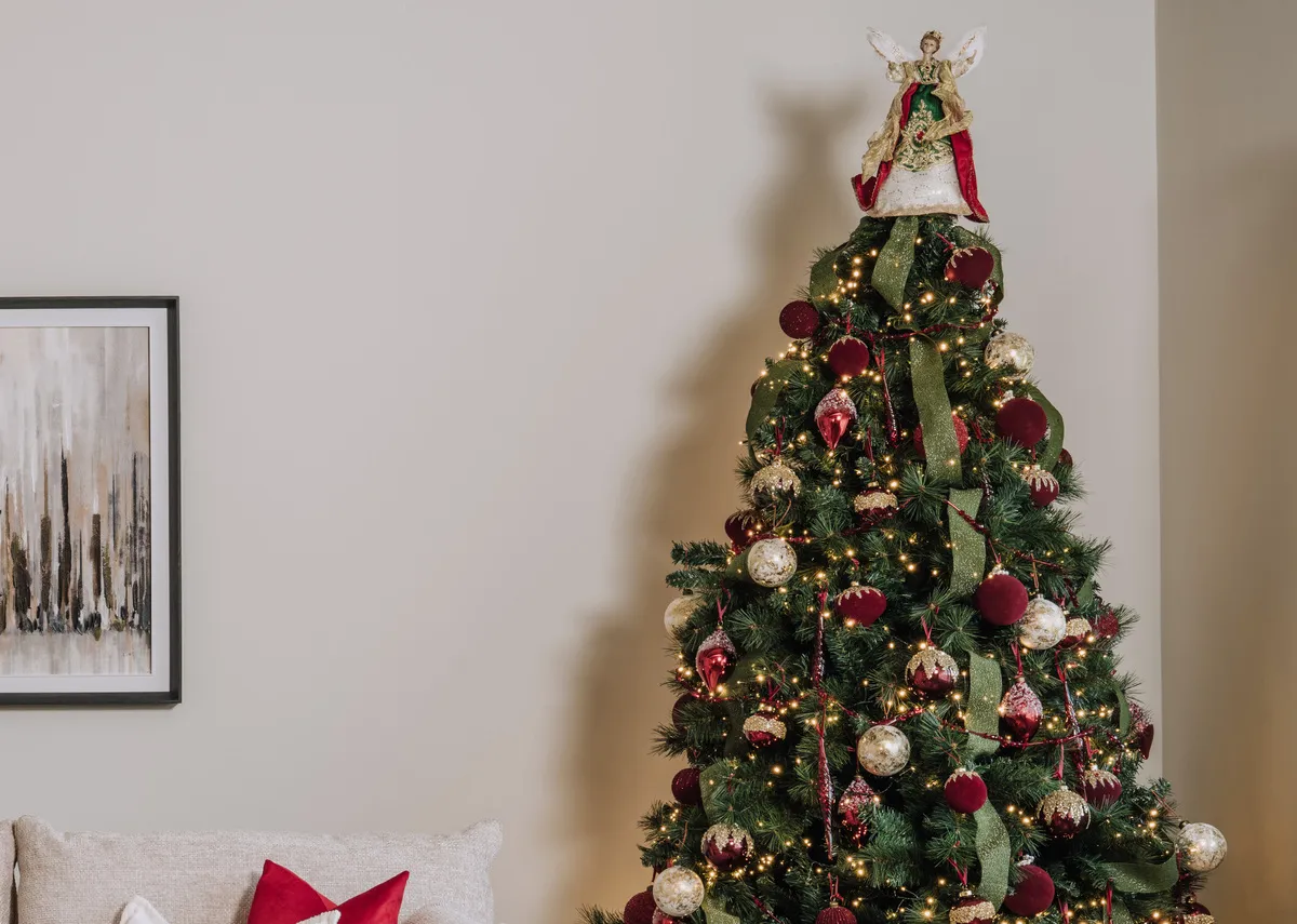 A lifestyle image of the Angel topper with a selection of red and gold baubles on a sherwood christmas  tree