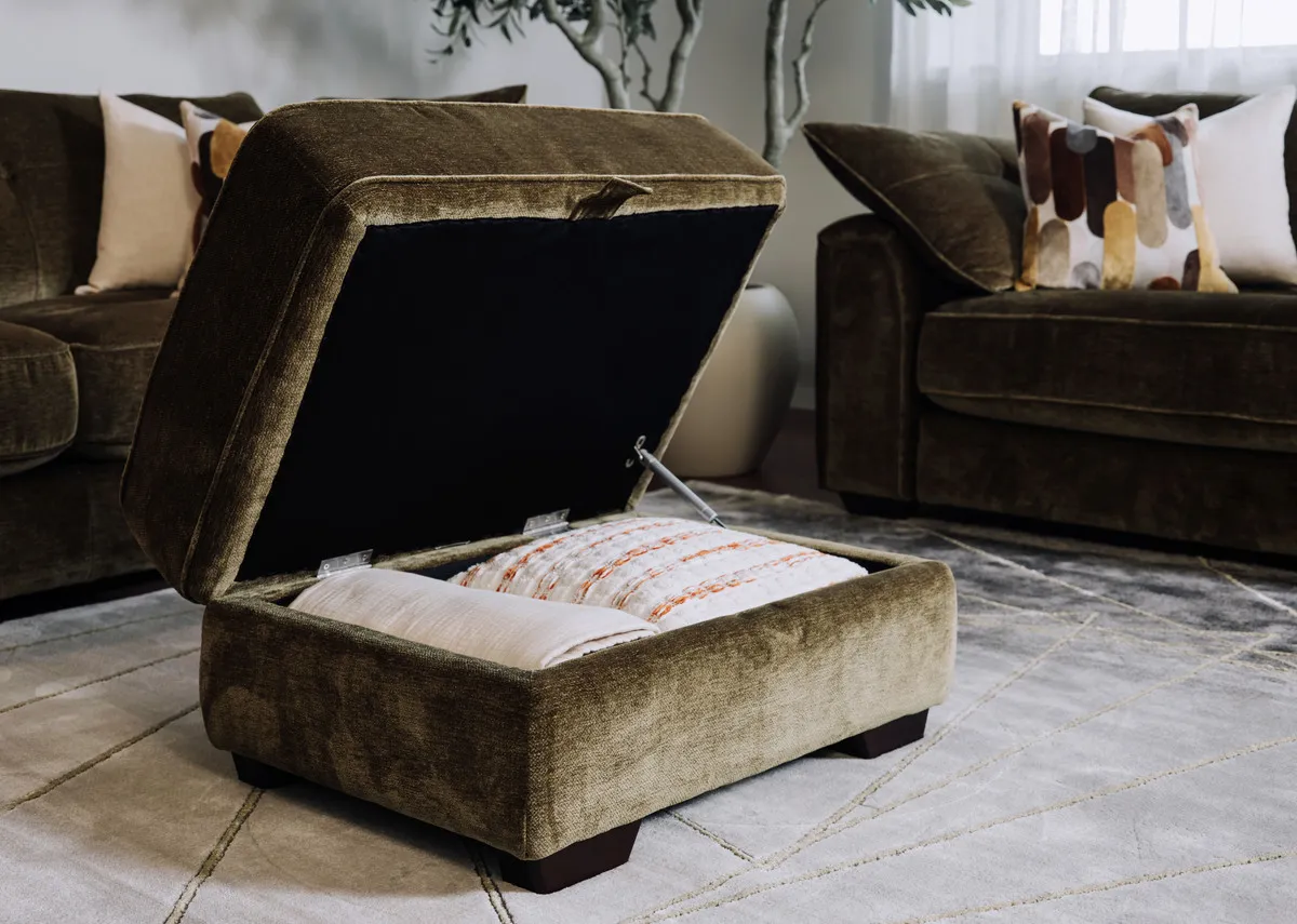 A lifetsyle image of the Darcy olive green footstool open showing hidden storage fitting a cushion and blanket.