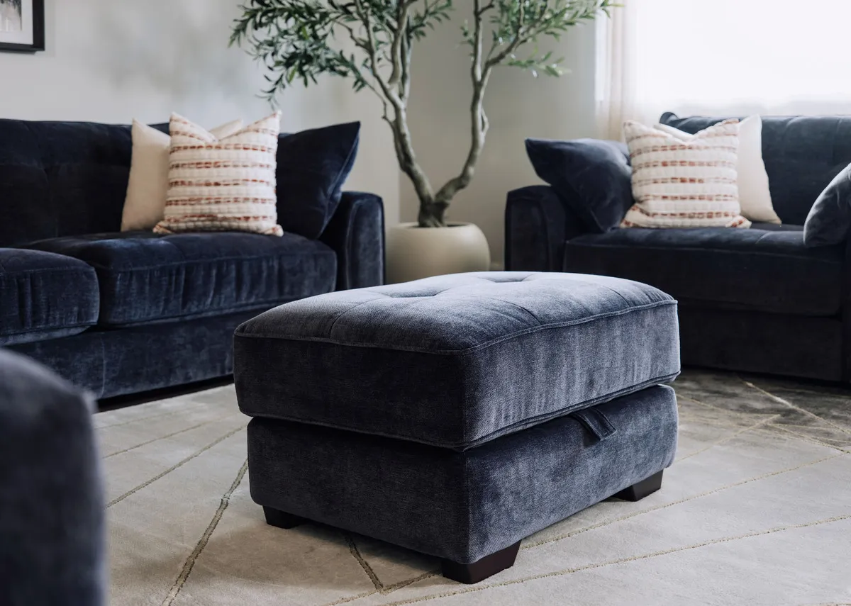 A lifetsyle image of the Darcy denim blue footstool closed as a seat with tufted button detailing.