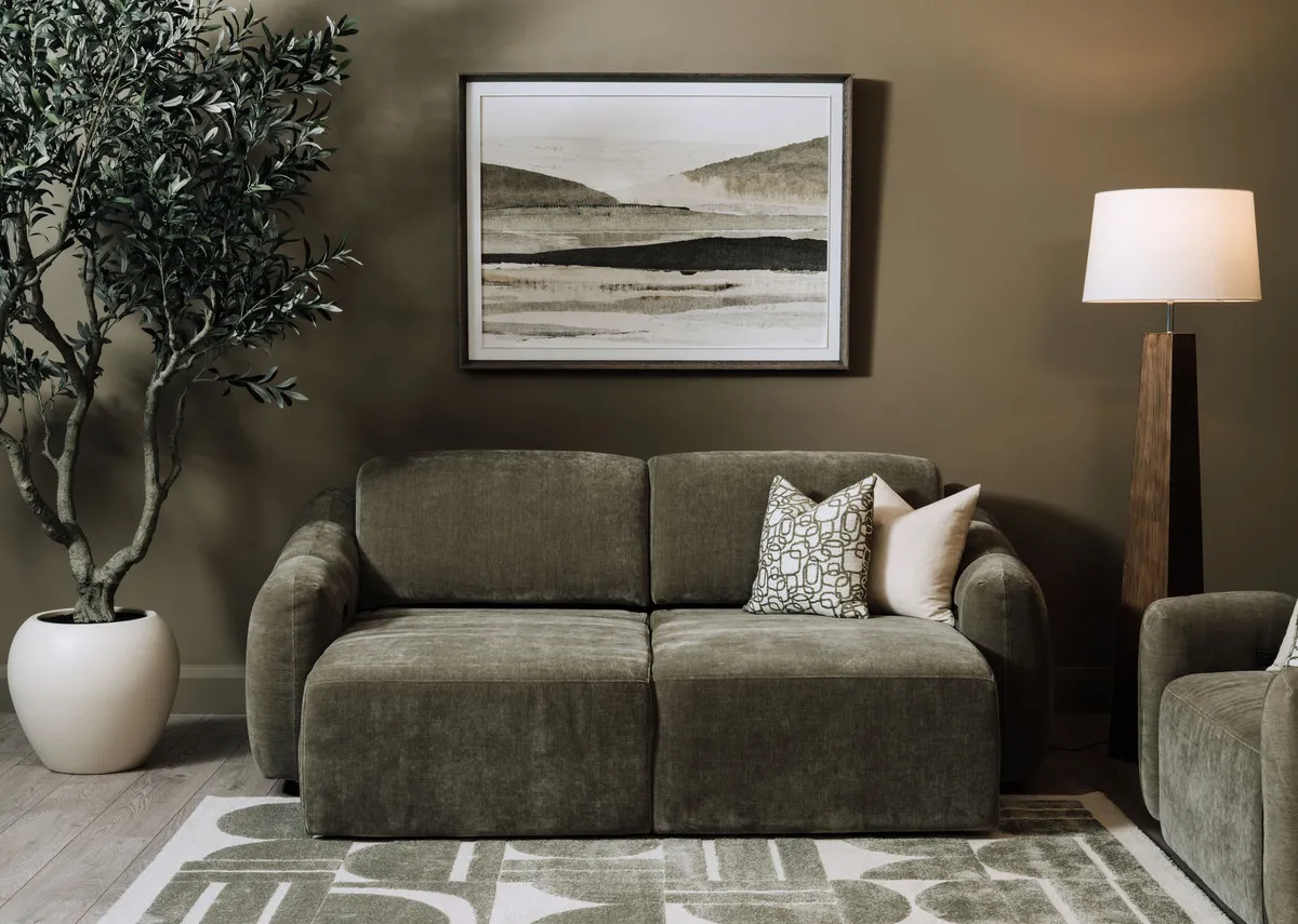 A lifestyle image of the Eleanor green 2 seater with both sides as a cinema chaise with Morning Haze painting and Eleanor armchair.