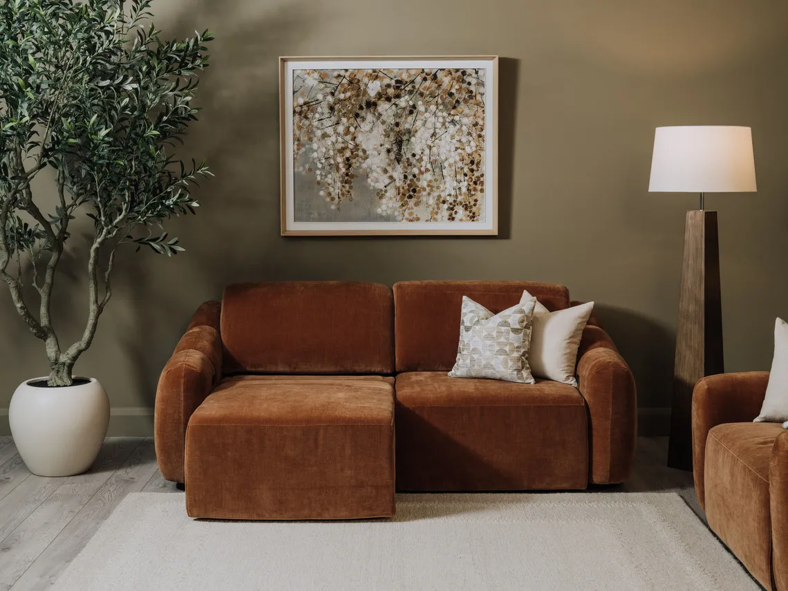 A lifestyle image of the Eleanor rust 2 seater with right side as a chaise with Bliss painting and Eleanor armchair.