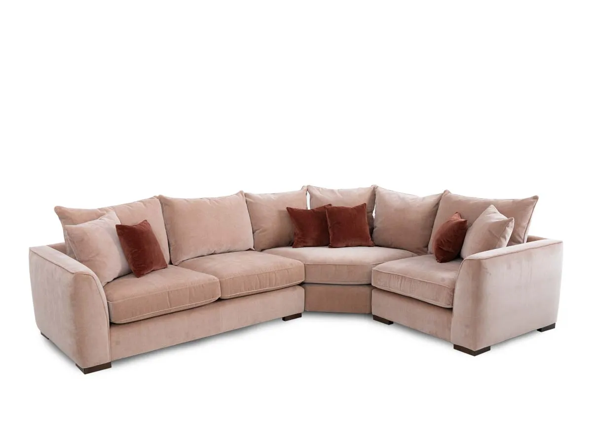 An LAF pink fabric corner sofa with rust cushions from Lucius range. Angled view of corner on left arm.