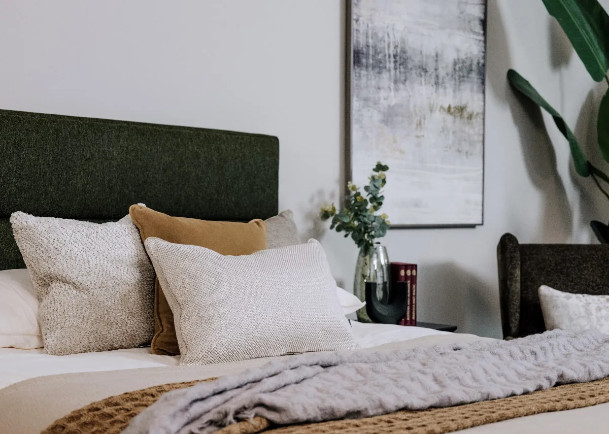 A lifestyle image of the ebony green headboard with a selection of cushions
