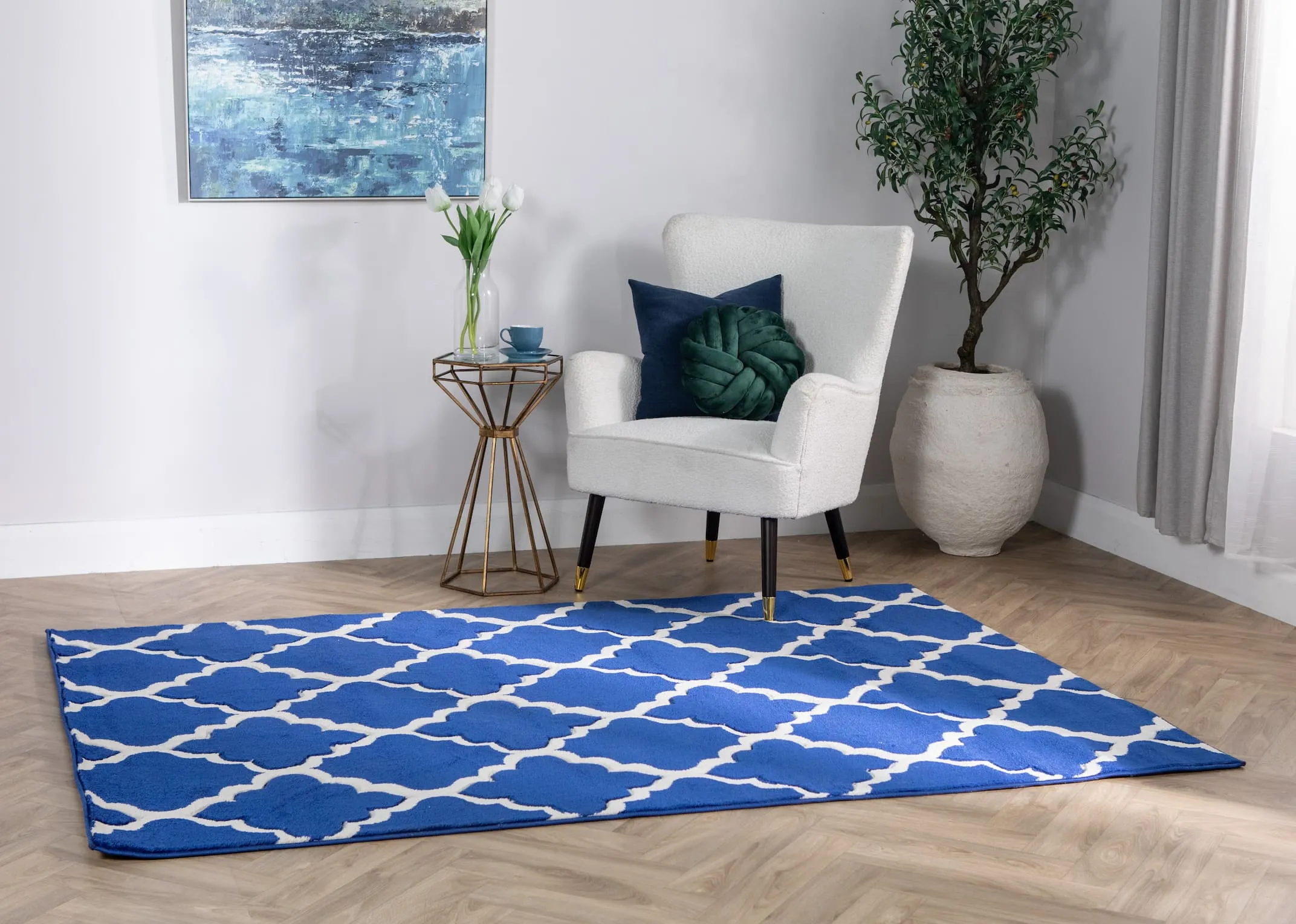 A lifestyle image of the Delia navy blue rug with Shiraz chair and Hour glass table with Olive plant & gardez pot.