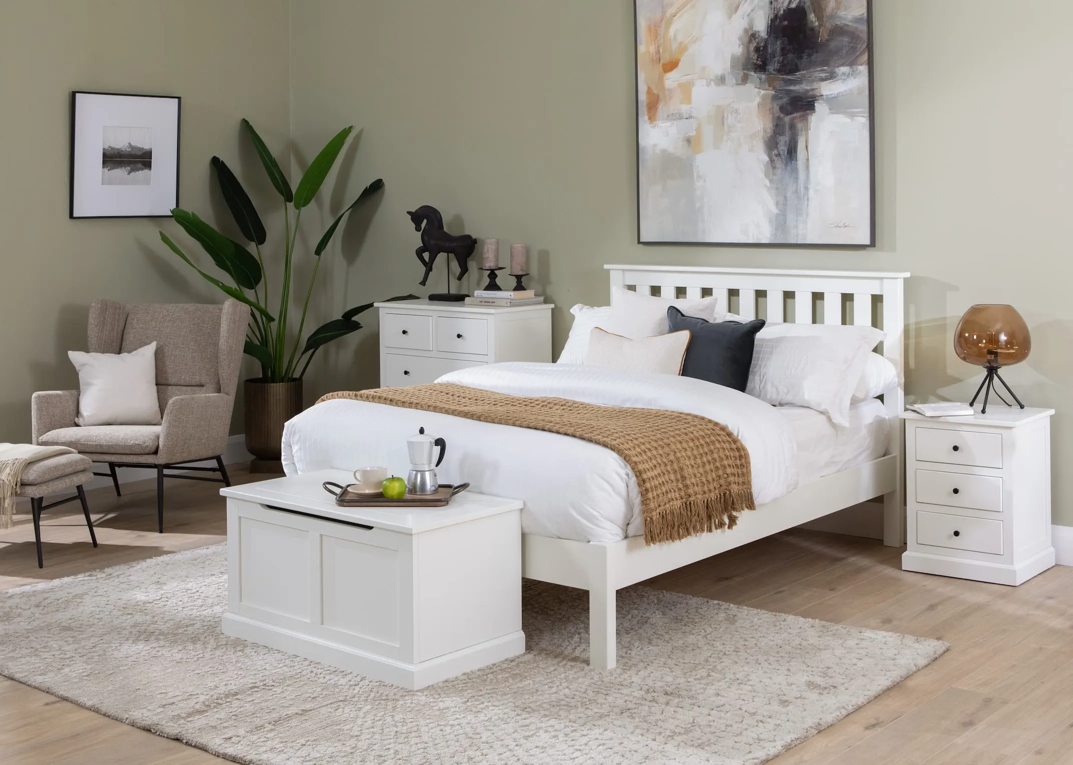 A lifestyle image of the White Atlas bedroom range including bedframe & chest of drawers & locker & blanket box with Boston cream chair