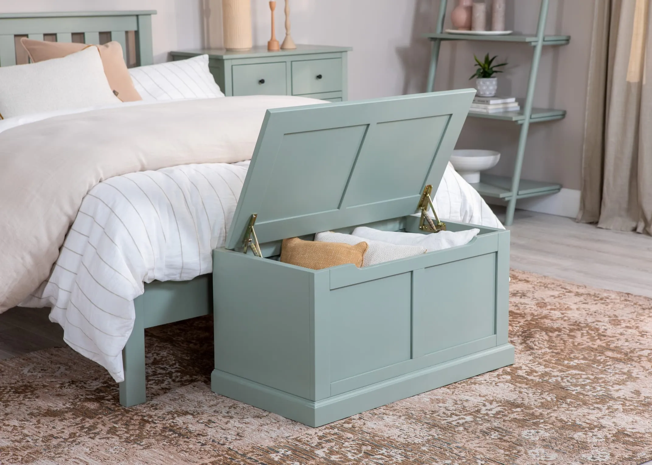 A lifetsyle image of the Atlas green bedroom range with blanket box open showing room for extra pillows and cushions