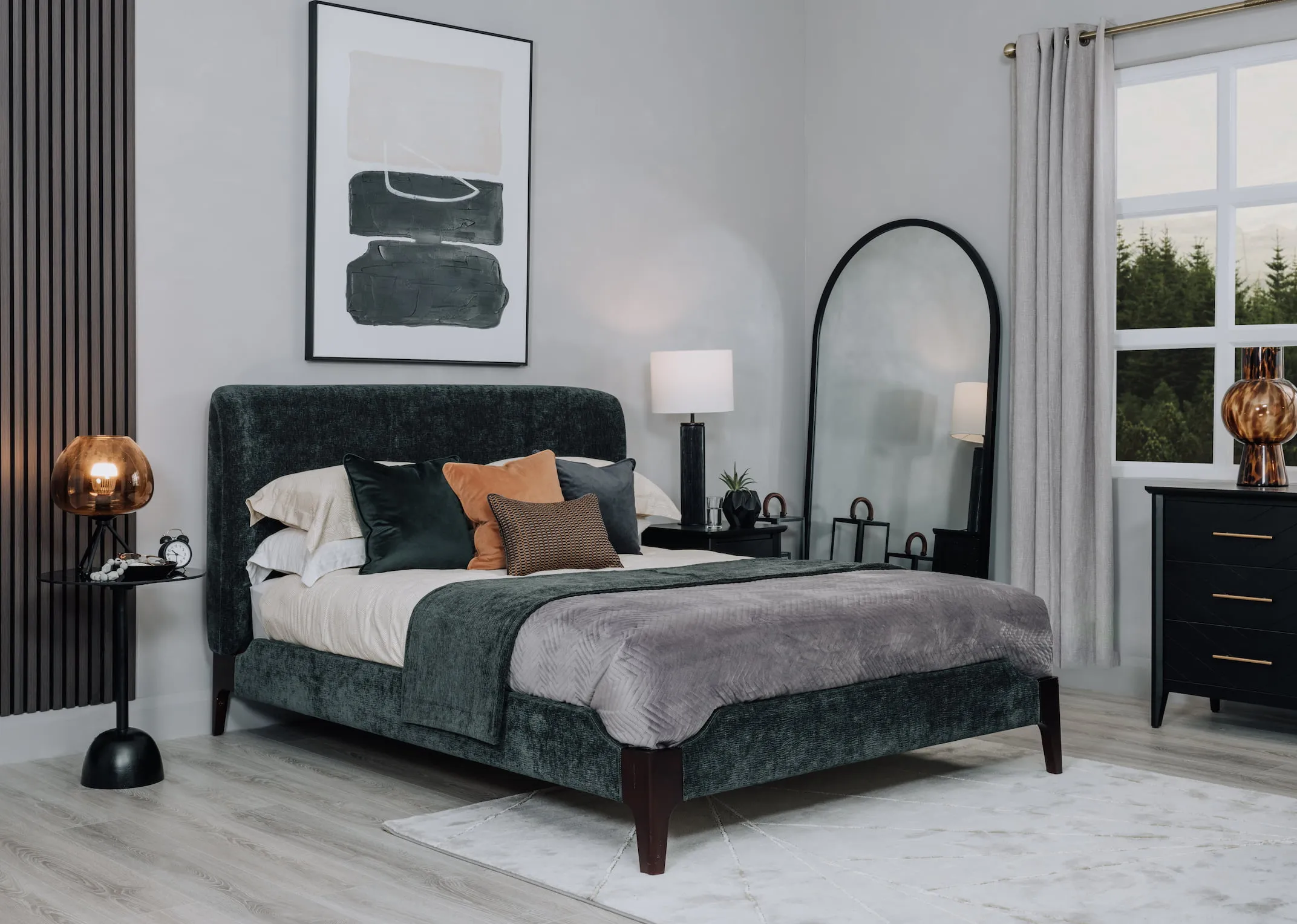 A lifestyle image of the Calm green bedframe with a selection of cushions and the chevron chest.