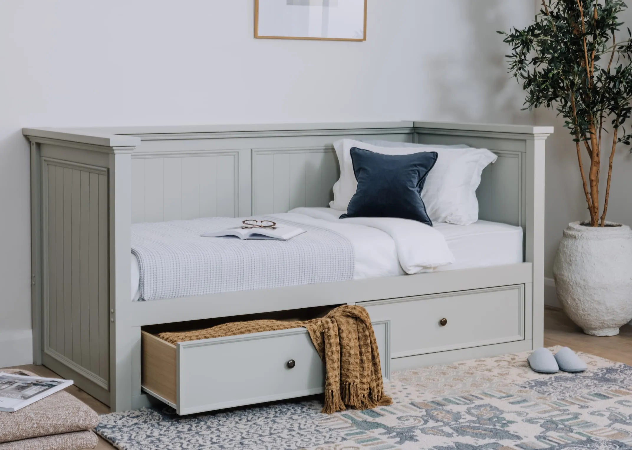 A lifestyle image of the Joseph Daybed with mattress and blankets and cushions with drawer open showing storage.