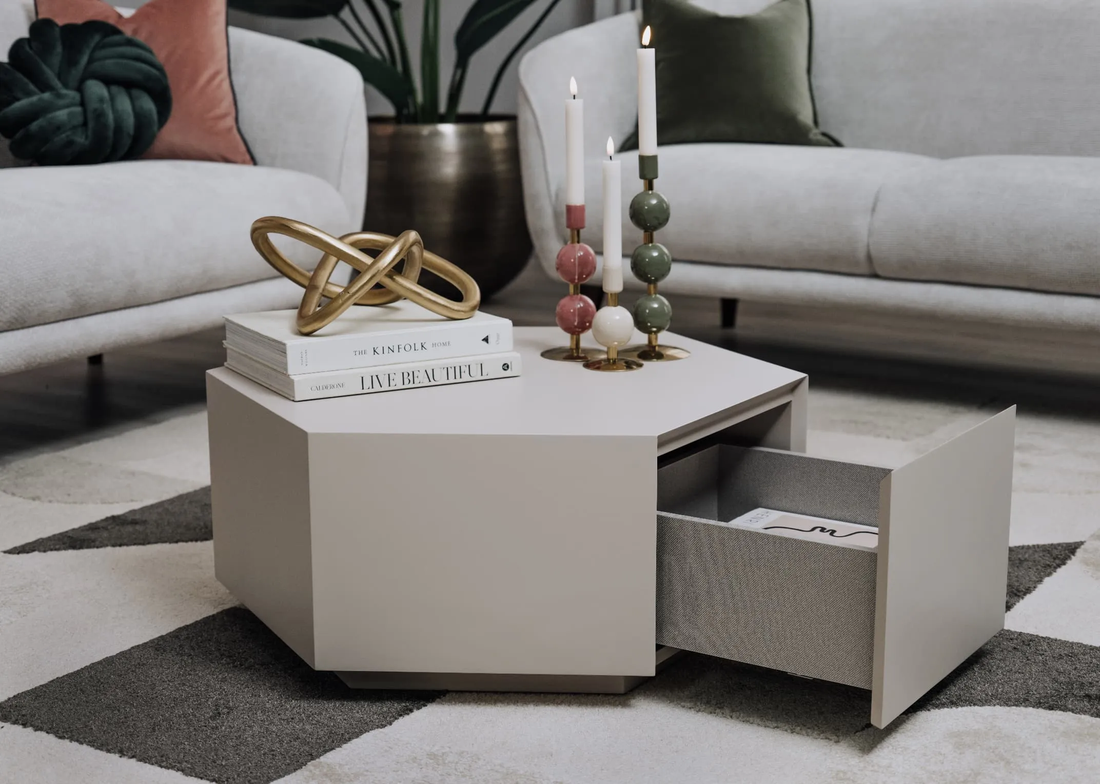 A lifestyle image of the Jonas Oatmenal coffee table with Amber sofa with drawer open showing room for books or candles and top dressed in candle holders and ornaments.