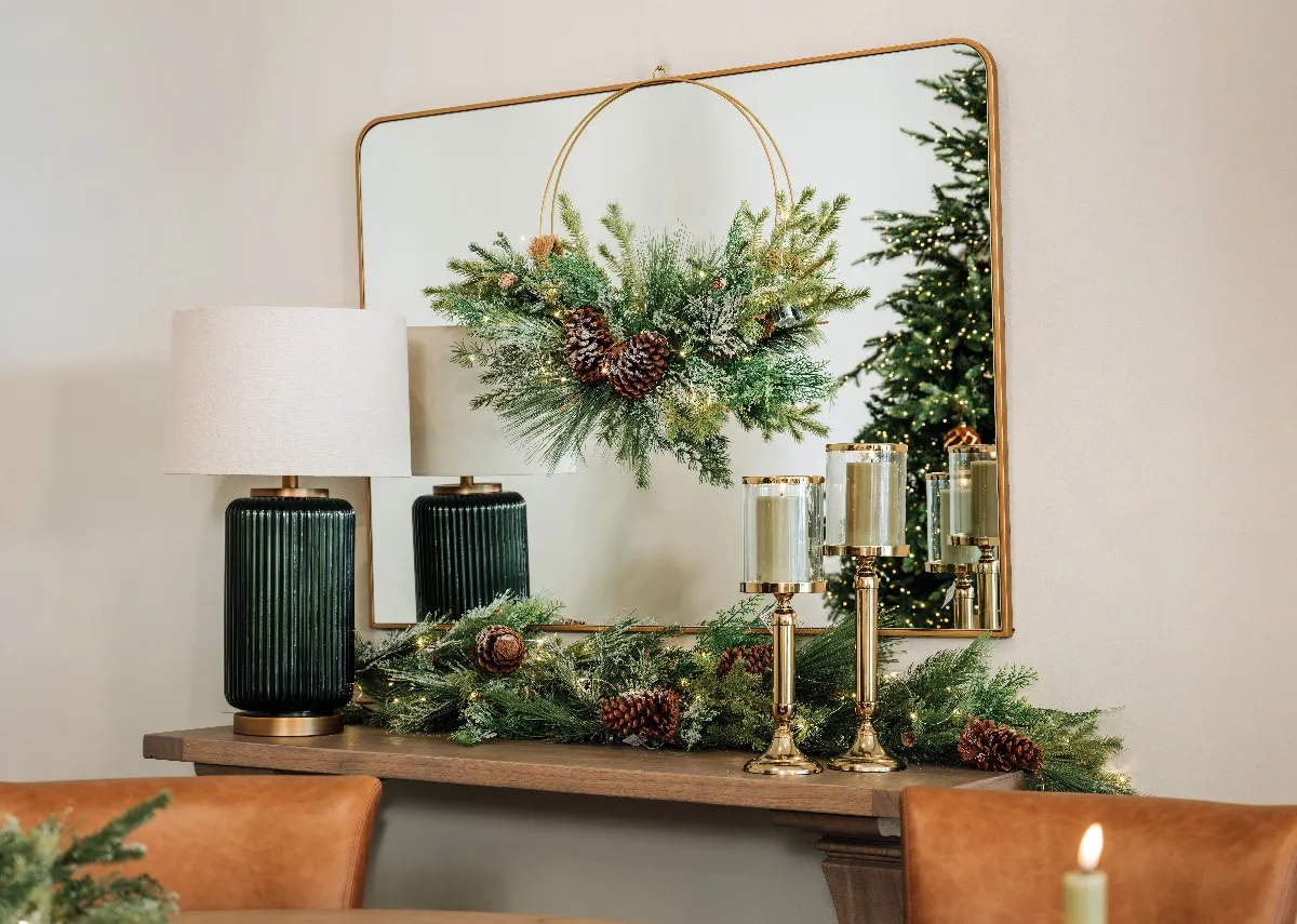 A lifetsyle image of the fern mirror with hanging wreath and green table lamp with frosted pine garland.