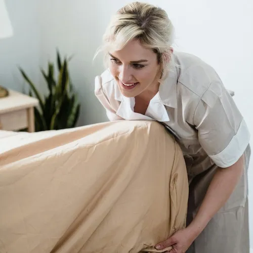Woman stripping bed sheets from mattress.
