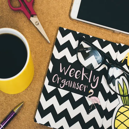 Weekly organiser notebook, coffee, scissors, phone, glasses.