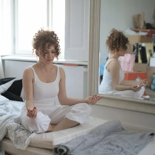 Woman sat meditating on mattress.