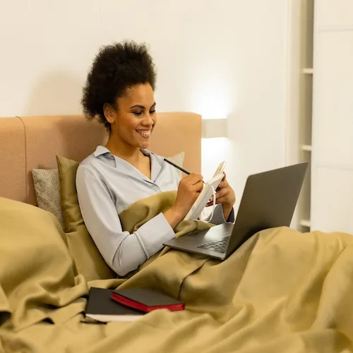 Woman working with laptop from her bed.