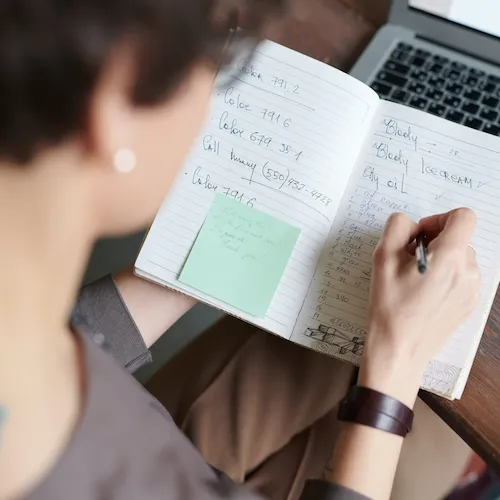 Woman writing list in notepad.